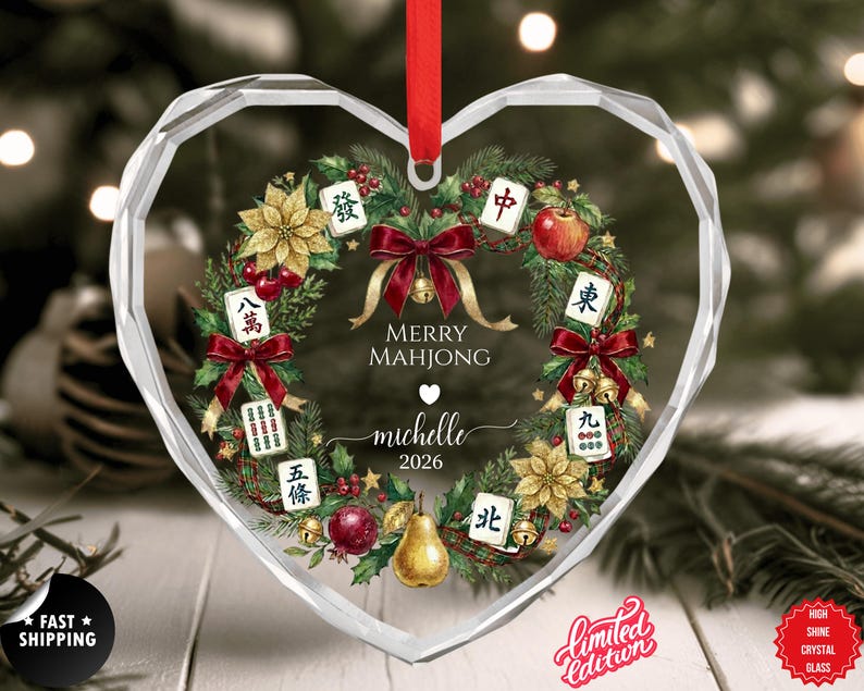 May include: Heart-shaped crystal glass ornament with a festive wreath design. The wreath features Mahjong tiles, red bows, and gold accents. Text reads "Merry Mahjong" and "Michelle 2026". A red ribbon is attached for hanging. Limited Edition.