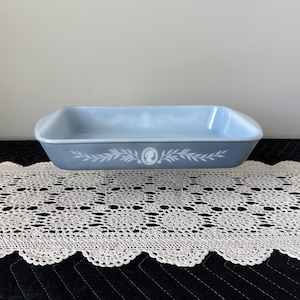 May include: A light blue rectangular baking dish with rounded corners. The dish features a white decorative design of a cameo and leaves. The dish is made of a durable material and is suitable for baking.
