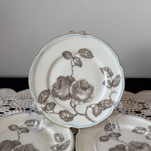 May include: A set of three ceramic mugs with a speckled, cream-colored glaze. Each mug features a different hand-painted floral design in shades of blue, green, and yellow. The mugs have a simple, rounded shape and a comfortable handle.