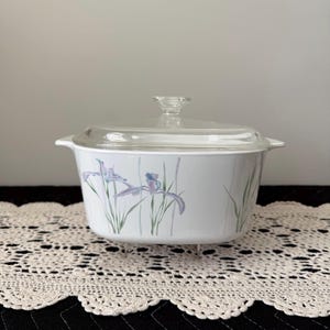 May include: White casserole dish with a clear glass lid. The dish features a floral design of purple irises and green stems. A classic piece for baking and serving.