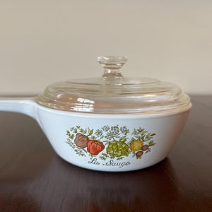 May include: White saucepan with a clear glass lid and a long handle. The side of the pan features a colorful illustration of vegetables and the text "La Sauge".