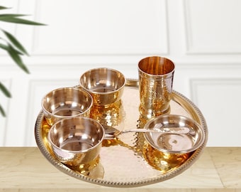 May include: A gold-toned metal dinnerware set with a hammered finish. The set includes a large plate, four bowls, a small plate, and a glass. 