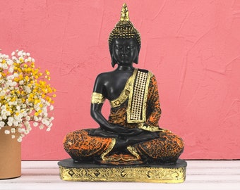 May include: Black Buddha statue with a gold trim and orange patterned robe sitting in a meditative pose on a gold base.