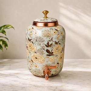 Puede incluir: Un dispensador de bebidas de cerámica con base azul claro y un patrón floral en tonos crema y marrón. El dispensador cuenta con una tapa de color cobre metálico con un remate dorado y un grifo de color cobre a juego en la base.