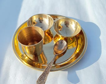 May include: A gold-colored metal serving set with a plate, two small bowls, a cup, and a spoon. The set is perfect for serving a small meal or snack.