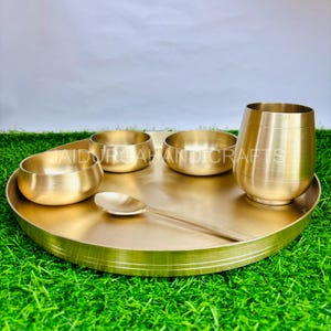 May include: A set of gold-coloured brass bowls and a cup, all sitting on a matching round tray. The set includes four small bowls and one larger cup.