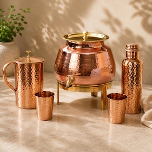 May include: A set of hammered copper drinkware including a large water dispenser with a brass lid and spigot on a metal stand, a pitcher with a lid, two small tumblers, and a tall water bottle, all featuring a textured, reflective metallic finish.