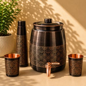Puede incluir: Un dispensador de agua metálico oscuro con un grifo de tono cobre etiquetado como Classinox, acompañado de una botella alta a juego y dos vasos. Cada pieza presenta un acabado negro con intrincados patrones geométricos de color cobre.