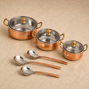 May include: A set of three round copper pots with hammered exterior textures, stainless steel interiors, glass lids with brass knobs, and matching side handles, accompanied by three matching copper-handled stainless steel serving spoons.
