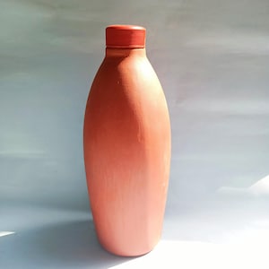 Puede incluir: Una botella de agua de terracota con tapa roja. La botella es de diseño tradicional y está hecha de arcilla.
