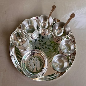 May include: A silver serving tray with a floral design and six silver bowls and two spoons. The bowls and spoons are arranged in a circle around the tray.