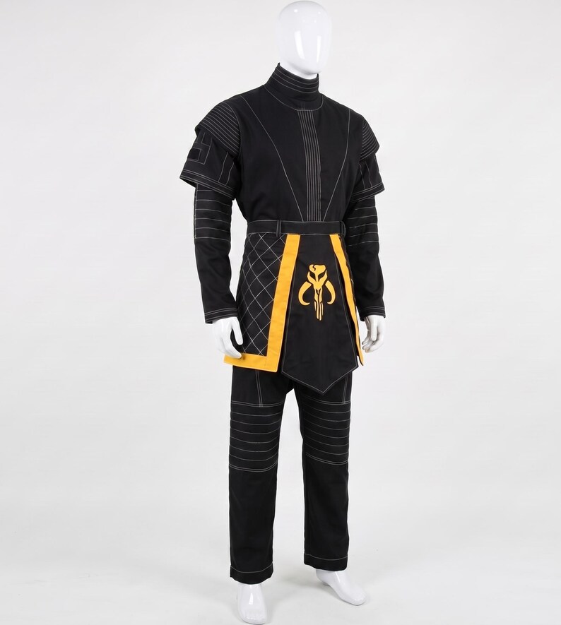 May include: A black long-sleeved tunic and pants set featuring white topstitching, a high collar, and short shoulder capes. A yellow waist sash with a quilted side panel and a central yellow Mythosaur skull emblem completes the ensemble.
