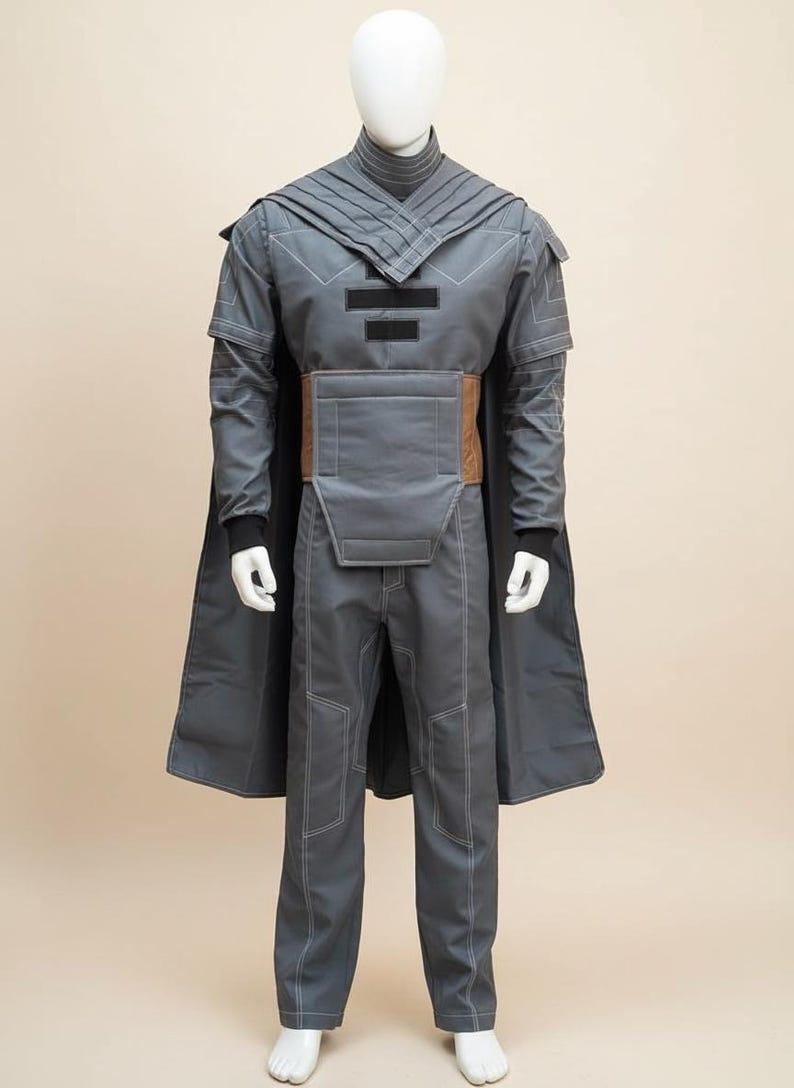 May include: A gray costume displayed on a mannequin. The outfit includes a long coat, pants, and a top with a high collar. A brown belt cinches the waist. White stitching details the seams. The costume has a futuristic or fantasy theme.