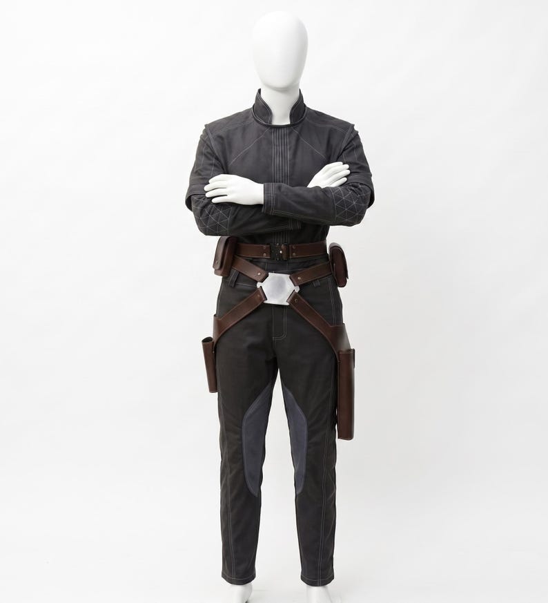 May include: A dark grey costume on a mannequin. The outfit features a jacket with diamond stitching on the shoulders, dark trousers with grey panels, and a brown belt with pouches and holsters. The mannequin's arms are crossed.