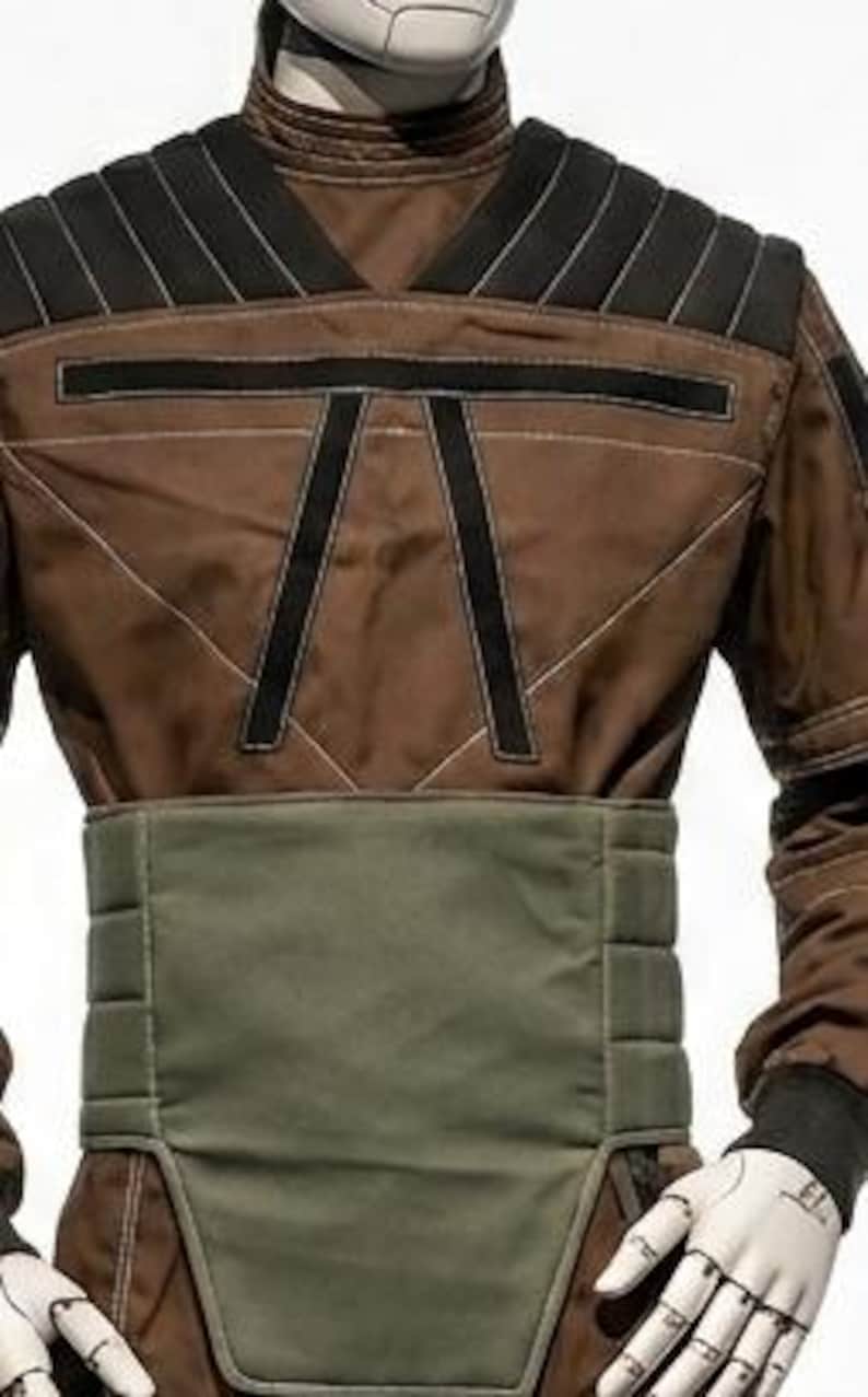 May include: A brown and black jumpsuit with a green waist belt. The jumpsuit has black accents on the shoulders and chest, with white stitching details. The sleeves are long, and the gloves are white.
