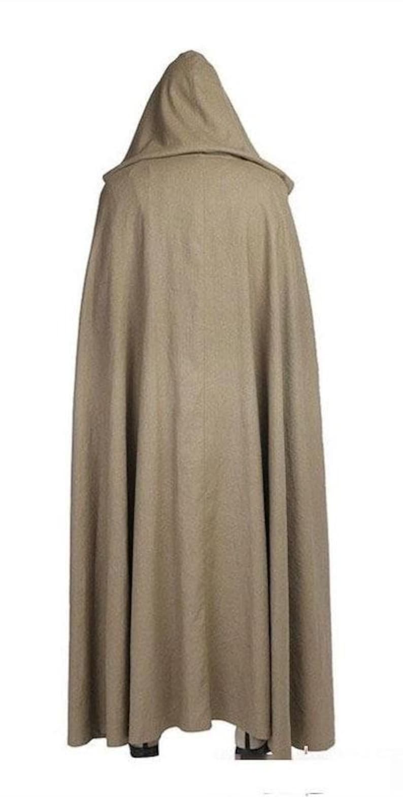 May include: A long, hooded cloak in a neutral tan color. The cloak has a full, flowing design and a large hood. The fabric appears to be a medium-weight material, suitable for cooler weather. The cloak is designed to be worn over other clothing.
