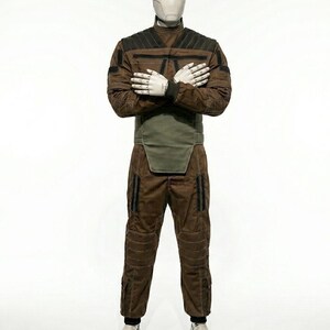 May include: A brown and black jumpsuit with a high collar, designed with quilted panels and pockets. The outfit includes a green waist protector and is displayed on a mannequin with a white head and hands. The mannequin is wearing white shoes.