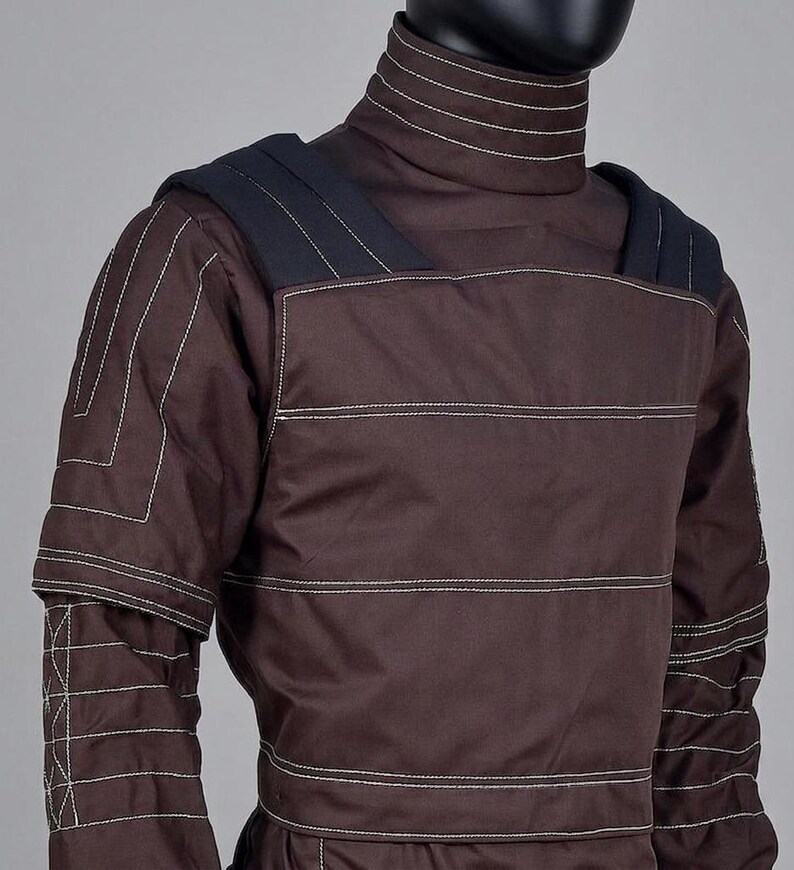May include: A brown quilted garment with white stitching, featuring a high collar and shoulder pads. The design includes horizontal and vertical stitching patterns. The garment is displayed on a mannequin, showcasing its structured design.