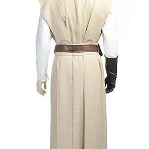 May include: A beige Jedi costume, featuring a long robe, a tabard, and a brown belt. The costume includes a white undershirt, brown gloves, and matching pants. The outfit is displayed on a mannequin against a white background.