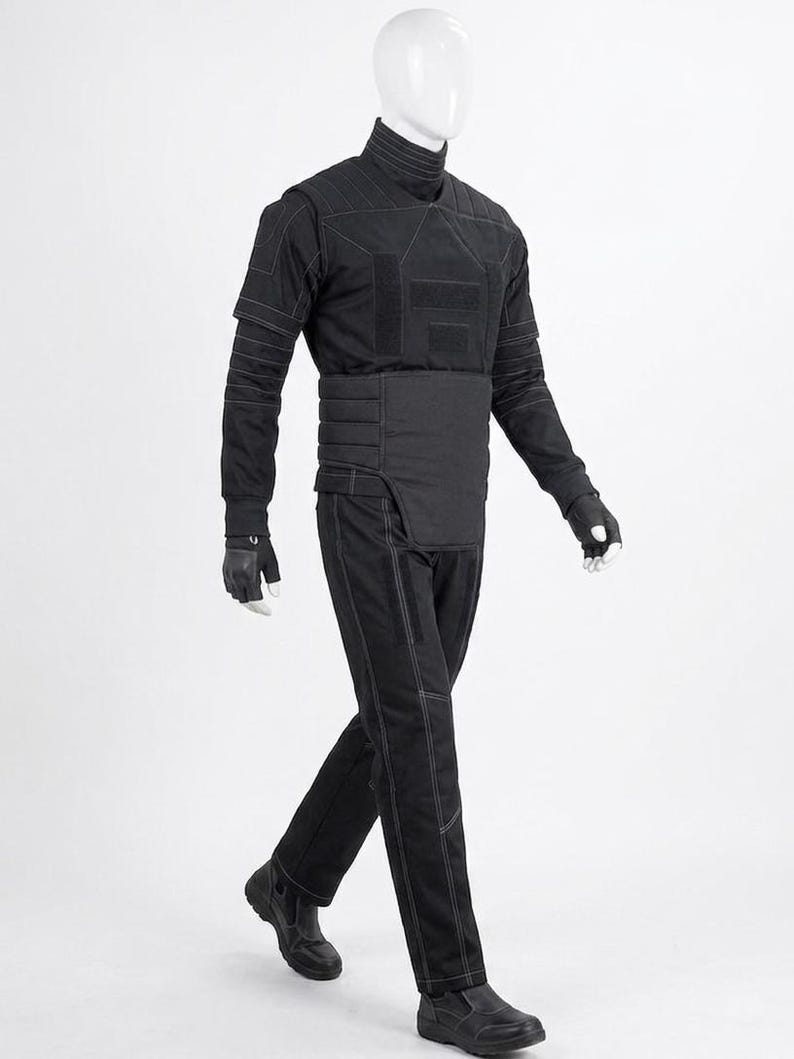 May include: A black tactical outfit displayed on a mannequin. The outfit includes a high-collared shirt, padded vest, belt, pants, gloves, and boots. White stitching accents the seams of the clothing. The mannequin is set against a white background.
