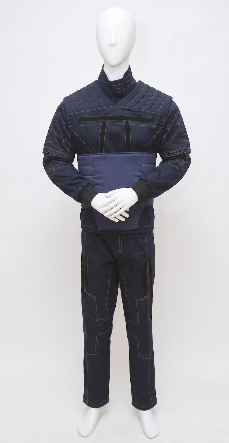 May include: Navy blue uniform displayed on a mannequin. The outfit features a high-collared jacket with quilted shoulders, a wide belt, and matching trousers. White stitching details the seams and pockets. The mannequin's hands are crossed at the waist.