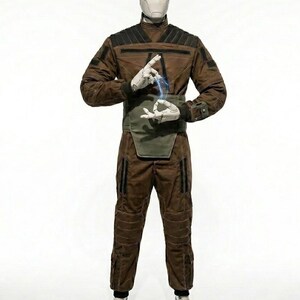 May include: A brown jumpsuit with black accents and a green waist protector. The outfit includes a high collar, multiple pockets, and padded sections on the knees. The figure is wearing white gloves and shoes. A blue energy effect is between the hands.