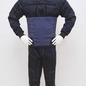 May include: A navy blue jumpsuit on a mannequin. The outfit has a high collar, quilted shoulder and chest panels, and a padded midsection. White stitching outlines the seams and pockets. The sleeves have black cuffs, and the trousers have geometric stitching.