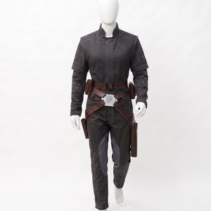 May include: A dark grey jumpsuit with a high collar, featuring a brown belt with pouches and a silver buckle. The sleeves have quilted detailing, and the trousers have grey accents. This costume is displayed on a mannequin.