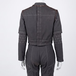 May include: Dark grey two-piece outfit. The jacket features brown leather detailing on the shoulders and collar, with geometric stitching on the sleeves. The trousers have matching stitching. The outfit is displayed on a mannequin.