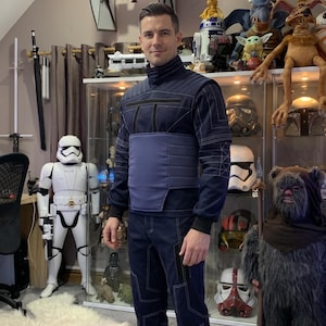 May include: A navy blue Star Wars-themed costume with white stitching and a matching vest. The costume is worn by a person standing in a room filled with Star Wars memorabilia, including a Stormtrooper figure and a TIE fighter model.