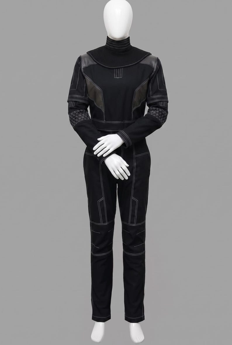 Peut inclure: Combinaison noire avec des d&eacute;tails de couture blancs, pr&eacute;sent&eacute;e sur un mannequin. La tenue pr&eacute;sente un col montant, des empi&egrave;cements aux &eacute;paules et des motifs g&eacute;om&eacute;triques sur les manches. Le pantalon a des empi&egrave;cements aux genoux et des coutures blanches.