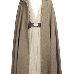 May include: A full-length costume featuring a hooded cape in a muted brown color. The costume includes a cream-colored tunic, a brown belt with a light blue oval buckle, and matching brown shoes. The outfit is designed to resemble a Jedi costume.