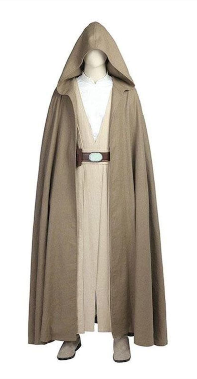 May include: A full-length costume featuring a hooded cape in a muted brown color. The costume includes a cream-colored tunic, a brown belt with a light blue oval buckle, and matching brown shoes. The outfit is designed to resemble a Jedi costume.