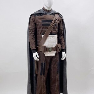 May include: A brown and black costume with a grey cape. The costume includes a long-sleeved shirt, trousers, and a belt with a pouch. The cape is draped over the shoulders. The costume is displayed on a mannequin.
