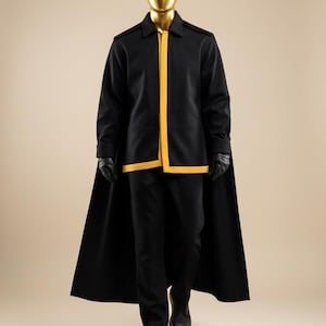 May include: A black jacket with a yellow front trim and a long cape back, paired with black trousers, black gloves, and black shoes. The outfit is displayed on a mannequin with a smooth, reflective gold-colored head and neck piece.