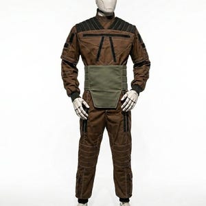 May include: A brown jumpsuit with black accents and a green waist belt is displayed on a mannequin. The outfit features black cuffs, white gloves, and white shoes. The mannequin has a white head.