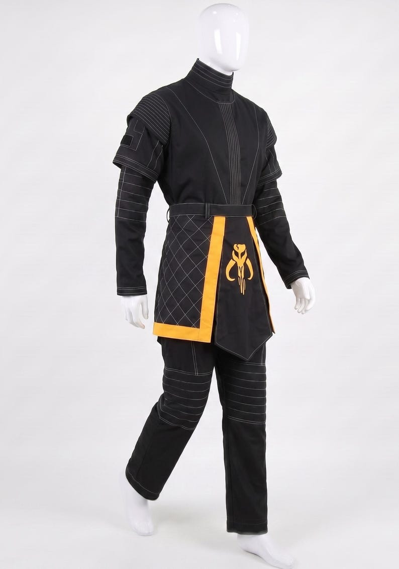May include: A black costume set featuring a high-neck tunic with white topstitching, quilted side panels, and matching trousers. A yellow waist sash with a central yellow emblem featuring a stylized helmet design is worn over the tunic.