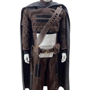 May include: A brown and black costume with a grey cape. The costume features a long-sleeved top, trousers, and a belt with pouches. The top has black accents and a white panel. The cape is draped over the shoulders.