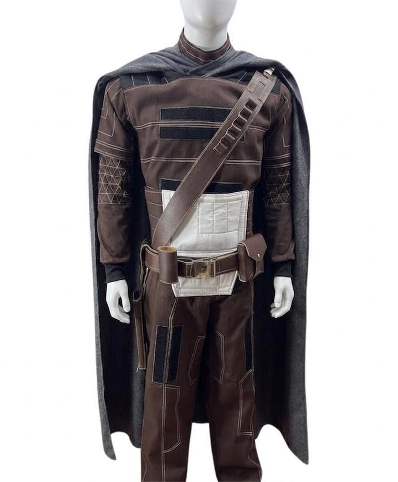 May include: A brown and black costume with a grey cape. The costume features a long-sleeved top, trousers, and a belt with pouches. The top has black accents and a white panel. The cape is draped over the shoulders.