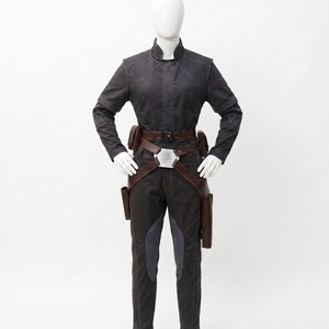 May include: A dark grey jumpsuit with a high collar, long sleeves, and a brown leather belt with pouches. The trousers have grey panels on the front. The outfit is displayed on a mannequin.