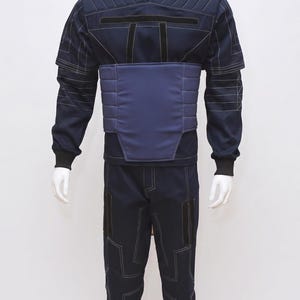May include: Navy blue jumpsuit with white stitching details, displayed on a mannequin. The outfit features a high collar, padded chest and waist panels, and matching trousers. The design includes black accents and a futuristic aesthetic.