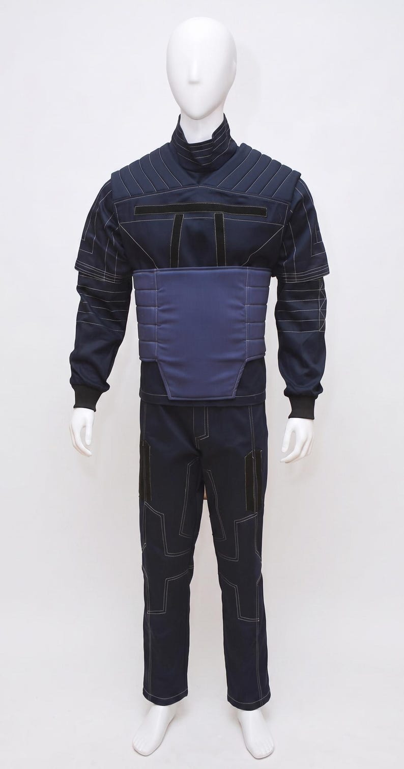 May include: Navy blue jumpsuit with white stitching details, displayed on a mannequin. The outfit features a high collar, padded chest and waist panels, and matching trousers. The design includes black accents and a futuristic aesthetic.