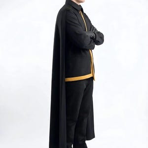 May include: A black long-sleeved jacket with a mustard yellow trim along the front opening and hem, paired with matching black trousers and a long black cape. The outfit includes black gloves and black leather boots with brown soles.