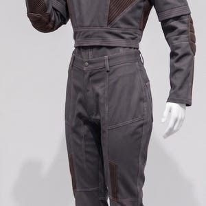May include: A grey jumpsuit on a mannequin. The outfit includes a cropped top with brown detailing on the shoulders and sleeves, and matching trousers. The design features stitched details and reinforced patches.