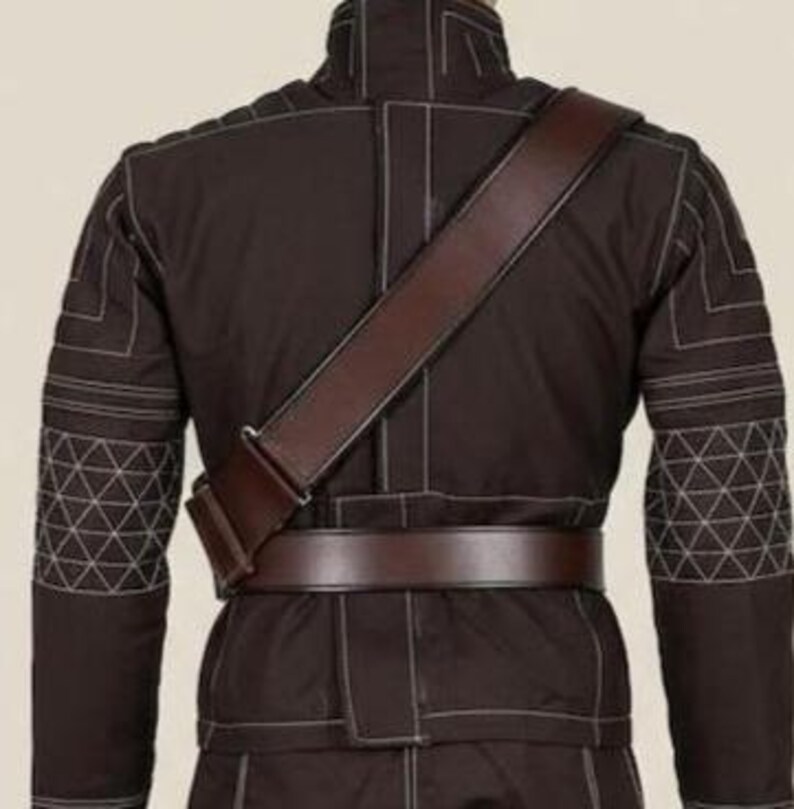 May include: A dark brown jacket featuring a high collar, long sleeves with white geometric stitching patterns, and a brown leather-like belt worn around the waist with a matching diagonal shoulder strap crossing over the back of the garment.