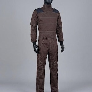 May include: A brown jumpsuit on a mannequin. The outfit has a high collar, reinforced shoulders, and white stitching. The long-sleeved top and trousers are made of a durable material. Black gloves and shoes complete the look.