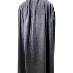 May include: A grey cape made of a soft fabric, draped over a mannequin. The cape is long, reaching to the mannequin's ankles, and has a high collar. The fabric has a subtle texture, and the cape is designed to flow.