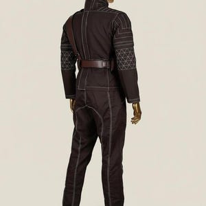 May include: A dark brown long-sleeved jumpsuit featuring white contrast stitching, a high collar, and a brown leather belt with a shoulder strap. The sleeves and shoulders display a geometric white grid pattern, and the garment is displayed on a mannequin.
