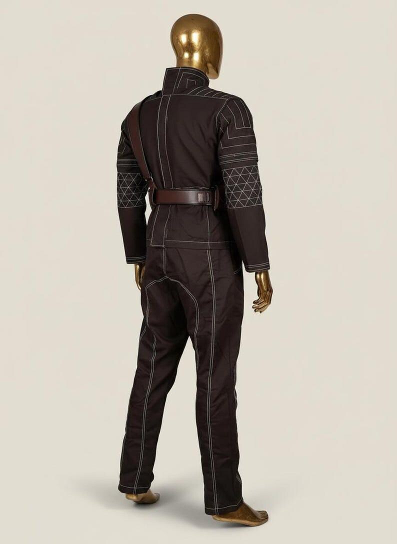 May include: A dark brown long-sleeved jumpsuit featuring white contrast stitching, a high collar, and a brown leather belt with a shoulder strap. The sleeves and shoulders display a geometric white grid pattern, and the garment is displayed on a mannequin.