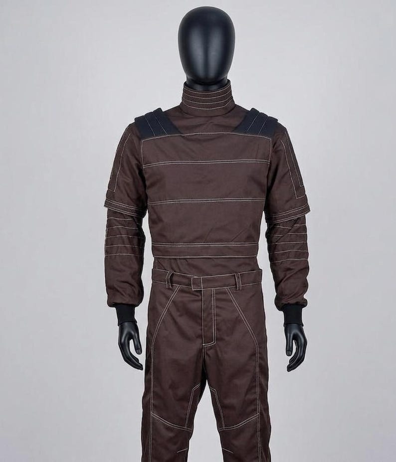 May include: Brown racing suit with white stitching details, displayed on a mannequin. The suit features a high collar, shoulder accents, and long sleeves with black cuffs. The trousers have a matching design with a belt and white stitching.
